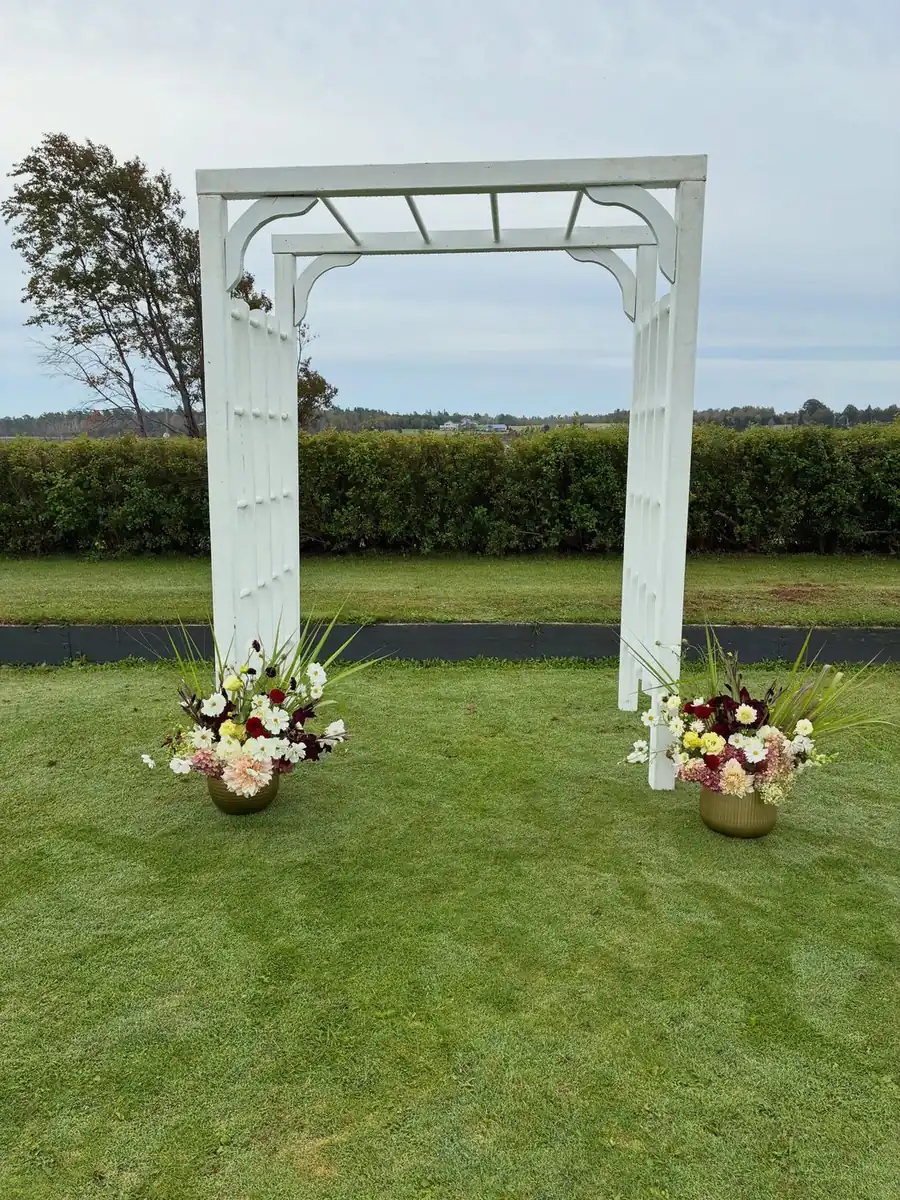 White wooden wedding arch with floral arrangements in burgundy and cream at its base