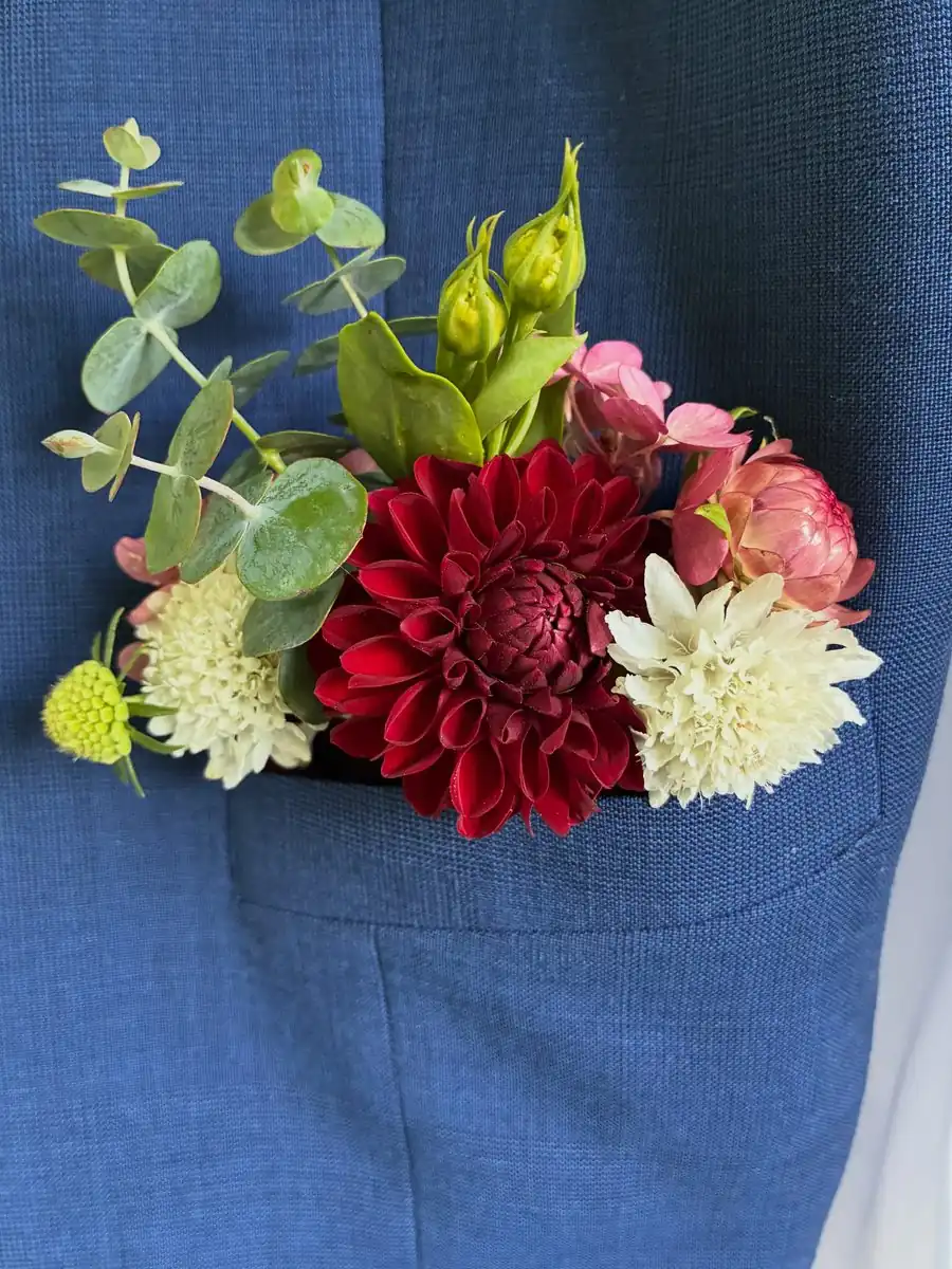 Burgundy, cream and pink wedding boutonniere with eucalyptus against a blue suit