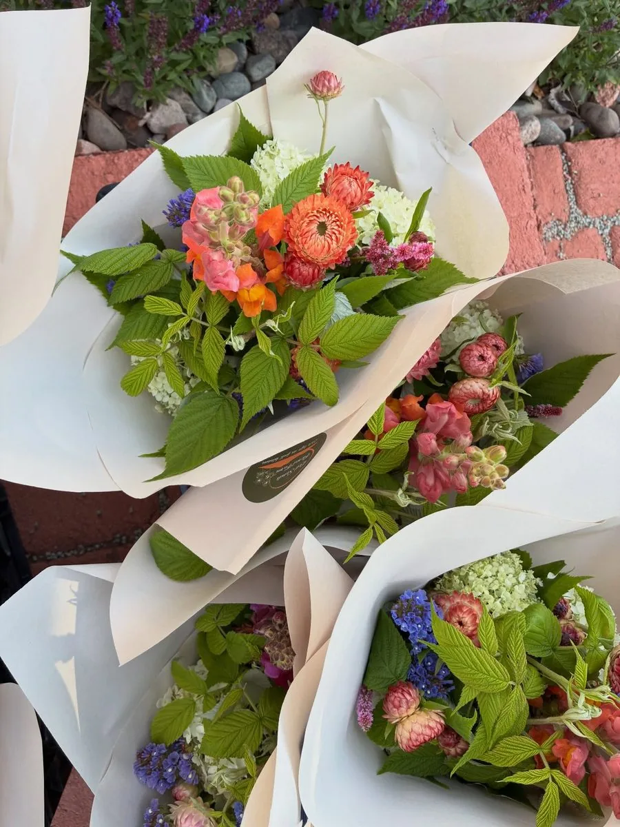 Wrapped market bouquets of pink and orange flowers with green foliage, seen from above